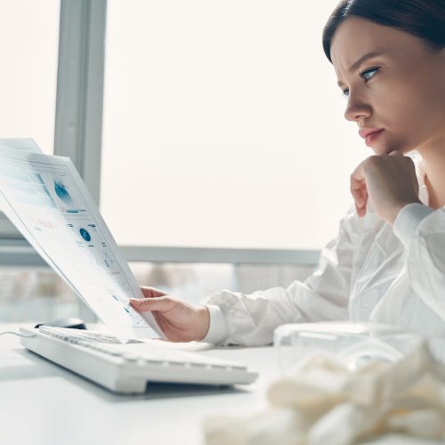 Side view of attractive young woman in protective suit studying results of medical tests at work